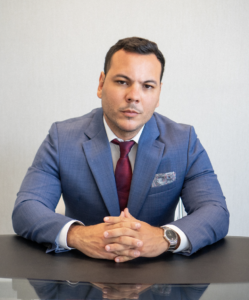 Owner of the Abreu Legal law firm in Doral, Florida, wearing a blue suit and seated at a desk in a professional office.